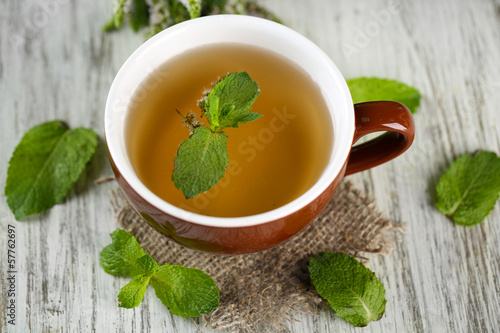 Cup of herbal tea with fresh mint flowers on wooden table