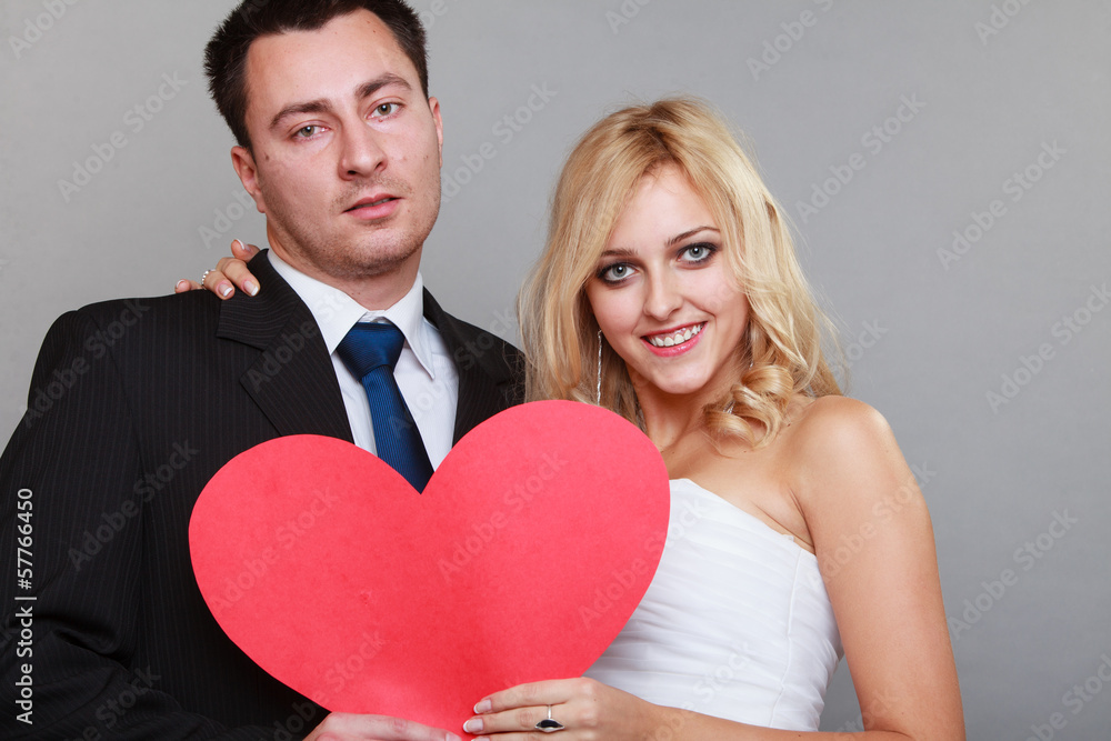 Portrait of happy bride and groom with red heart on gray Portrait of happy bride and groom with red heart on gray