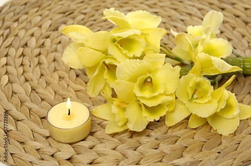 burning candle and branch yellow orchid on woven mat     
