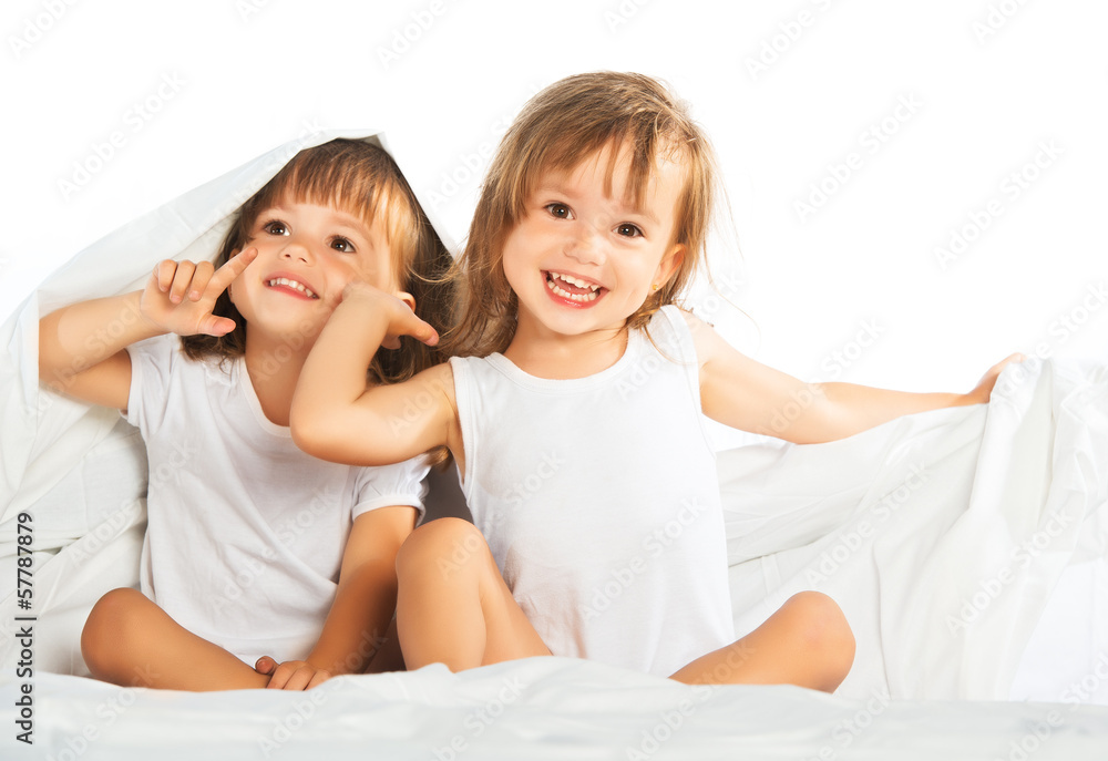 happy little girls twins sister in bed under the blanket having happy little girls twins sister in bed under the blanket having
