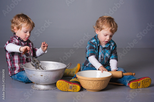 Cute blonde twins playing with cooking bowls and utensils