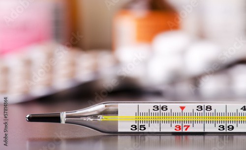 Mercury thermometer and medical pills on background