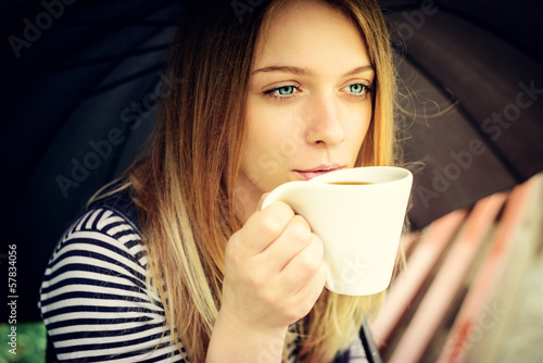 womanl drinks fragrant coffee with pleasure under umbrella