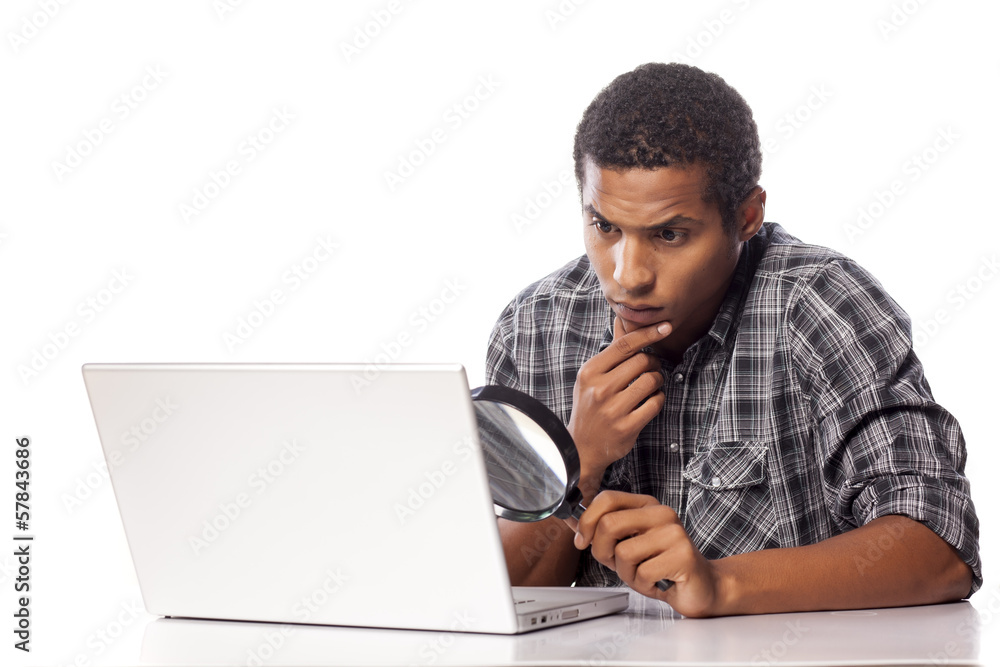 african man looking through a magnifying glass on his laptop african man looking through a magnifying glass on his laptop