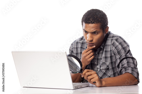african man looking through a magnifying glass on his laptop