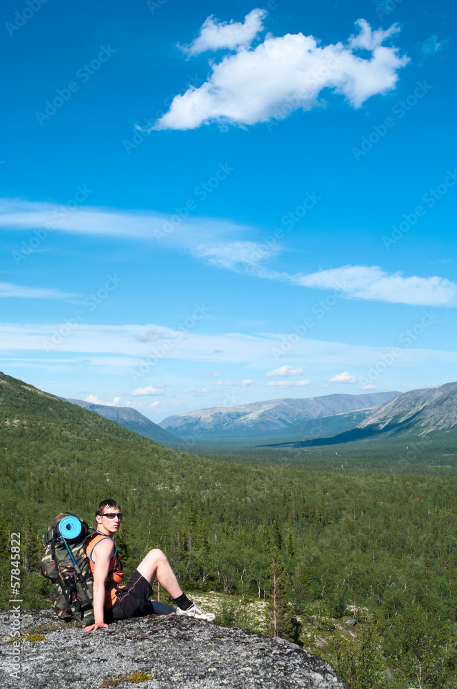 Man hiker with backpack sitting on top and looking at camera