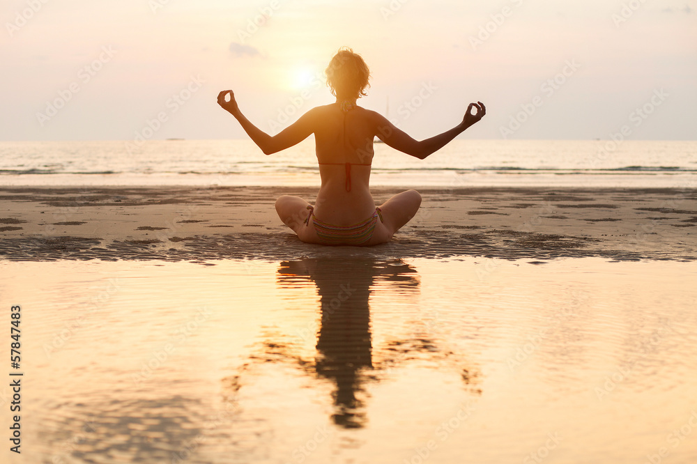 Yoga woman sitting in lotus pose on the beach during sunset