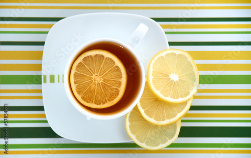 Cup with tea and lemon on colorful striped background