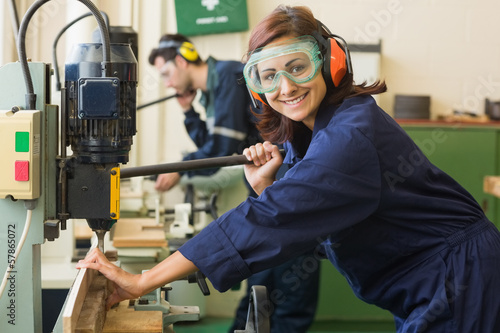 Smiling trainee with safety glasses drilling wood photo