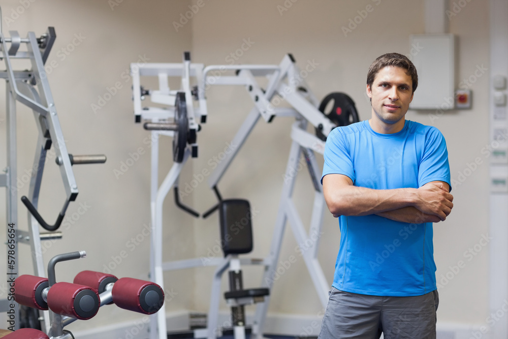 Smiling trainer with arms crossed against lat machine in gym Smiling trainer with arms crossed against lat machine in gym