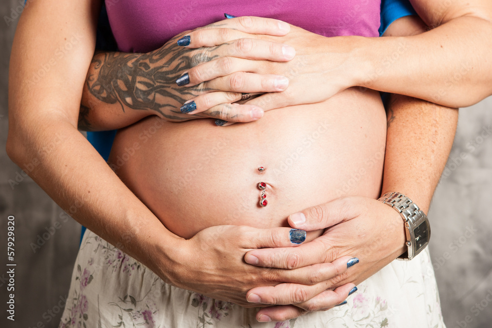 Tattoed man and woman interlock fingers over baby belly Tattoed man and woman interlock fingers over baby belly