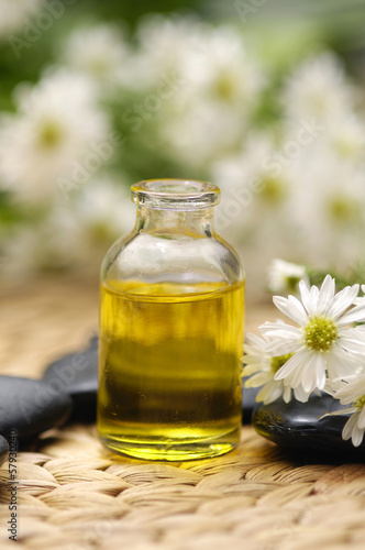 Massage oil with daisies flower and stones on wicker mat