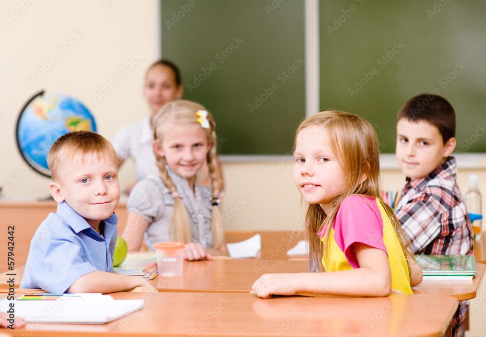 Portrait of schoolkids at workplace with teacher on background Portrait of schoolkids at workplace with teacher on background