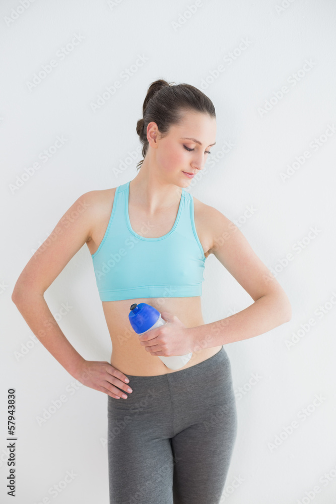 Toned woman holding water bottle against wall