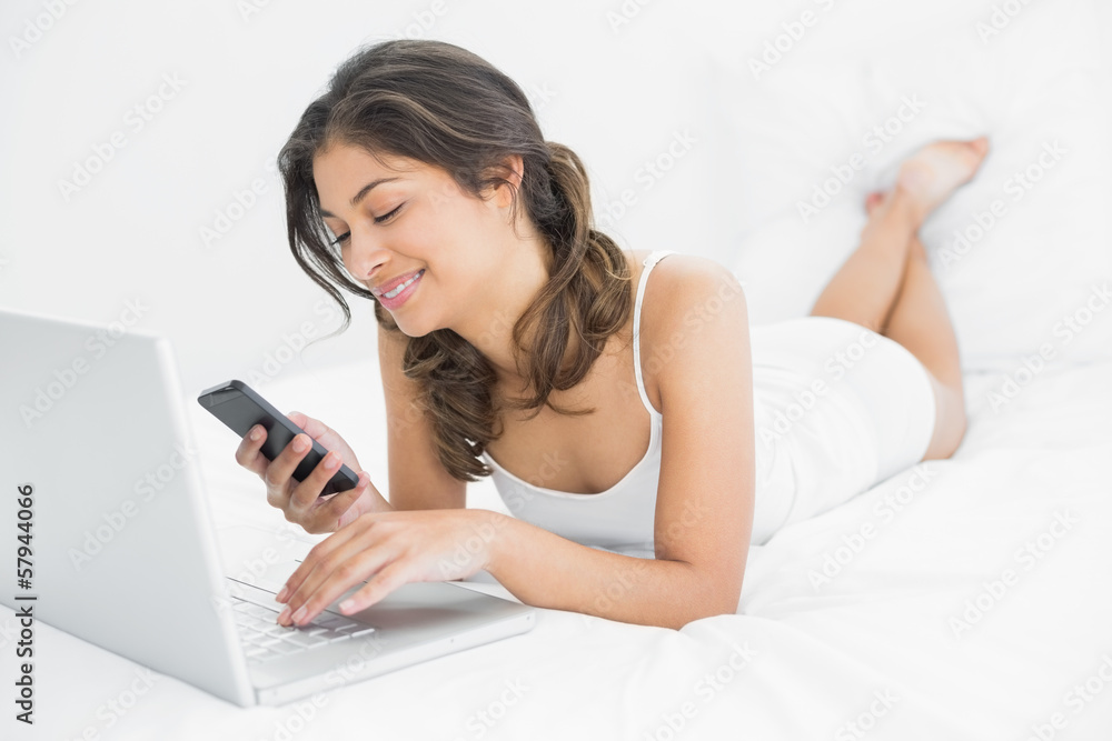 Casual woman using laptop while text messaging in bed Casual woman using laptop while text messaging in bed