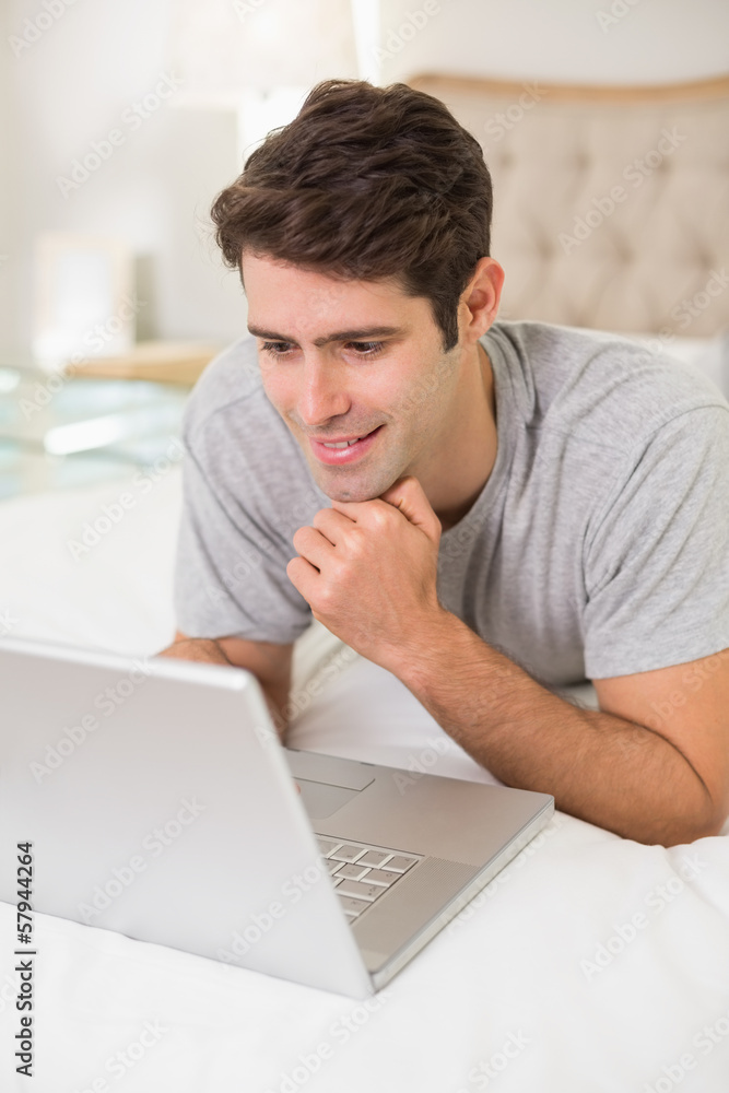 Casual smiling young man using laptop in bed Casual smiling young man using laptop in bed