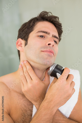 Handsome shirtless man shaving with electric razor