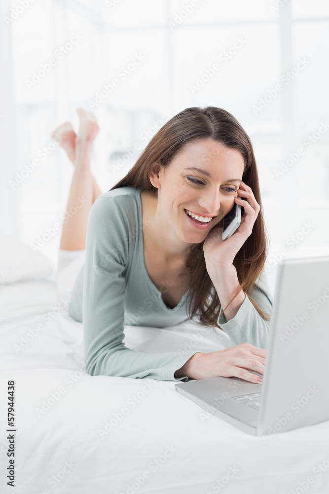 Smiling casual woman using cellphone and laptop in bed Smiling casual woman using cellphone and laptop in bed