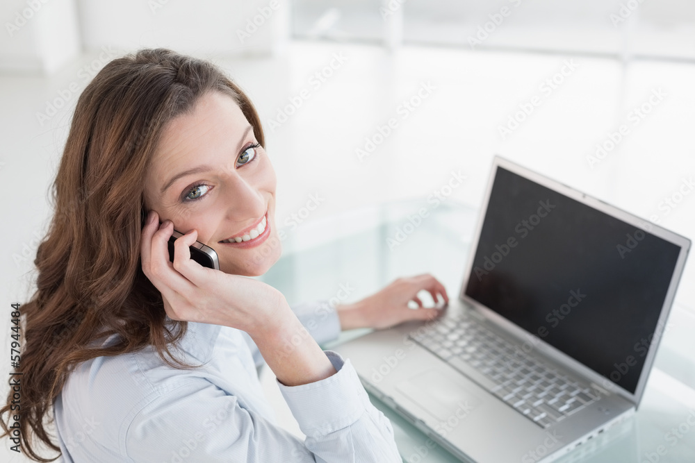 Brown haired businesswoman using laptop and cellphone in office Brown haired businesswoman using laptop and cellphone in office