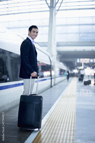 Businessman standing with a suitcase on the railroad platform by a high speed train in Beijing