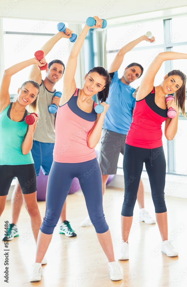 People lifting dumbbell weights with trainer in gym People lifting dumbbell weights with trainer in gym