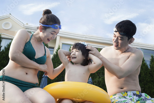 Smiling happy family helping son put on goggles by the poolside © xixinxing