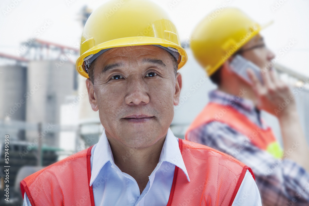 Two engineers in protective workwear working, looking at camera, outside of a factory Two engineers in protective workwear working, looking at camera, outside of a factory