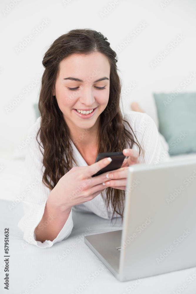 Smiling casual woman with cellphone and laptop in bed Smiling casual woman with cellphone and laptop in bed