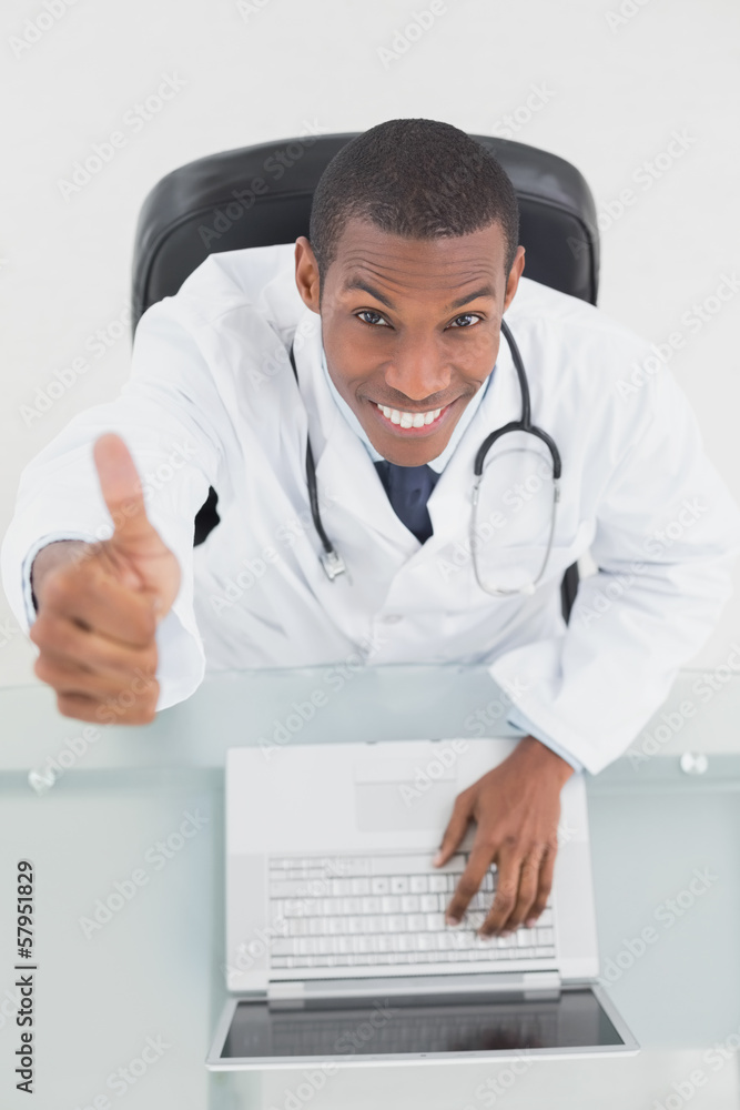 Overhead of smiling male doctor with laptop gesturing thumbs up Overhead of smiling male doctor with laptop gesturing thumbs up