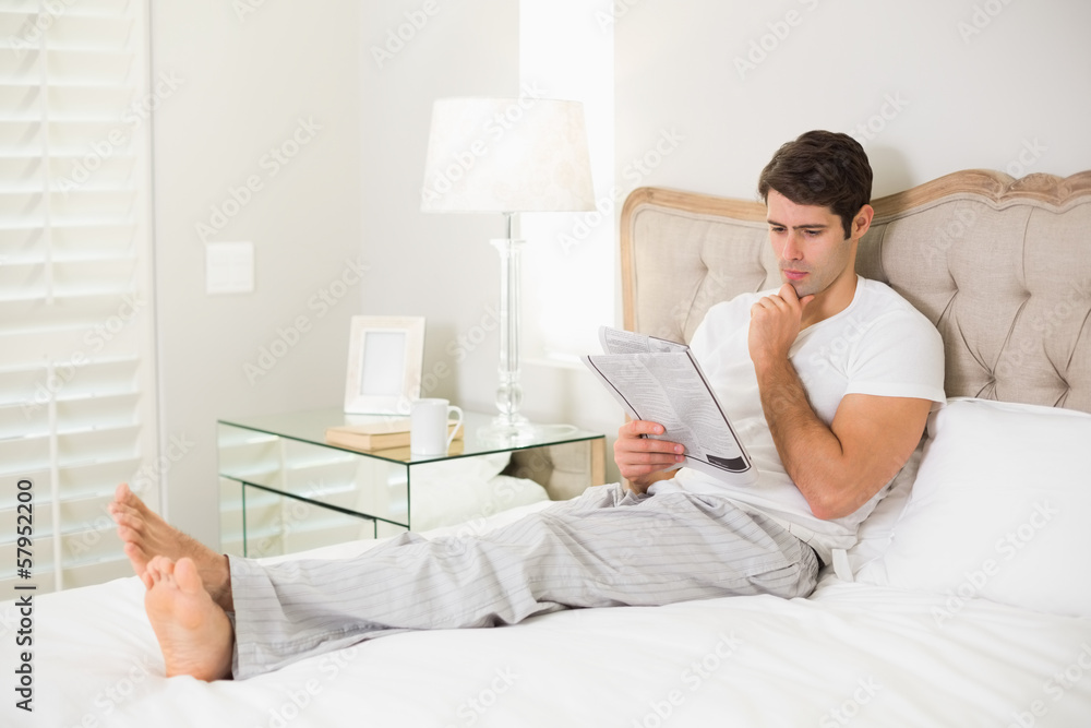 Casual man reading newspaper in bed Casual man reading newspaper in bed