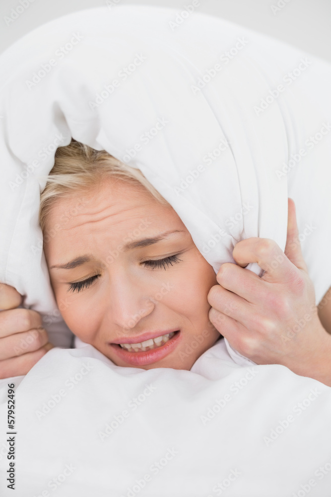 Displeased woman covering ears with pillow Displeased woman covering ears with pillow