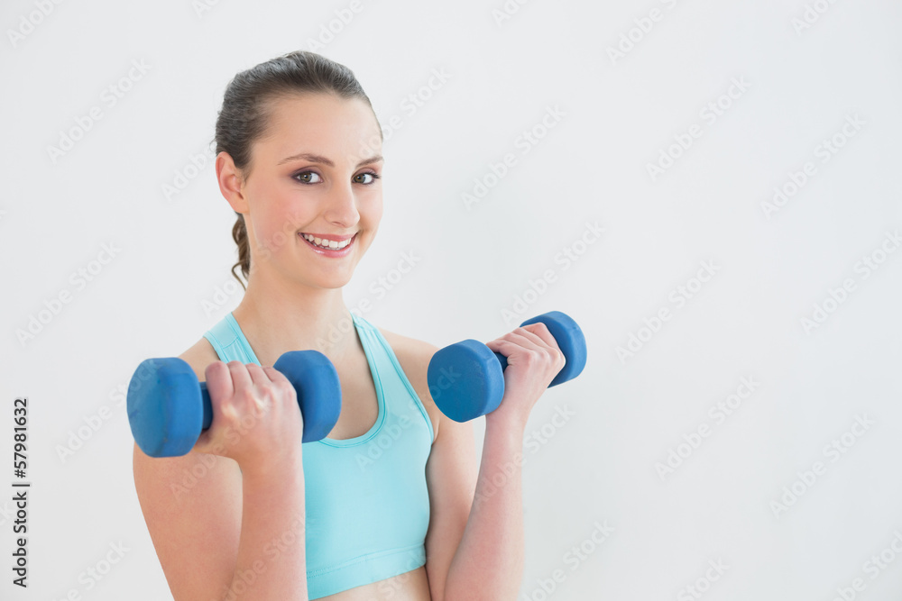 Smiling woman with dumbbells against wall Smiling woman with dumbbells against wall