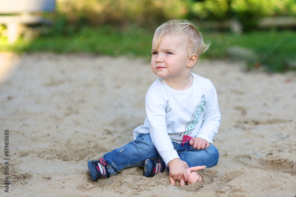 Cute baby girl playing in the playground sitting in the sand Cute baby girl playing in the playground sitting in the sand