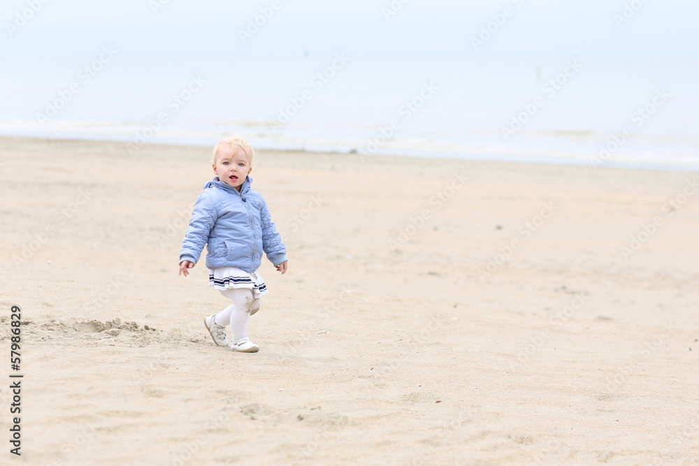 Funny little baby girl walks on peaceful sandy beach 