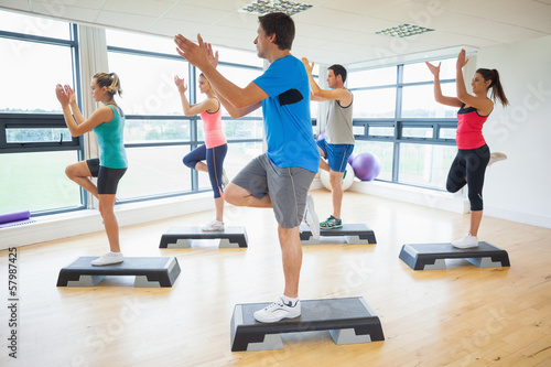 Instructor with fitness class performing step aerobics exercise