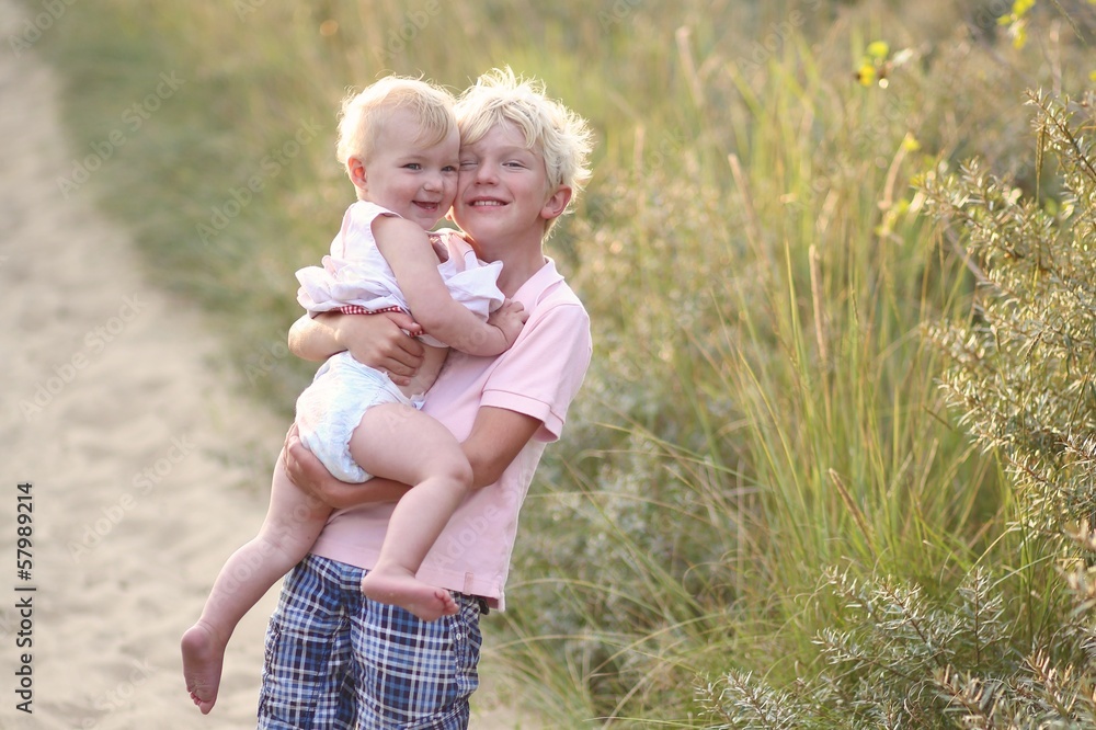 Fototapeta premium Loving teeneger boy holding his baby sister in the dunes