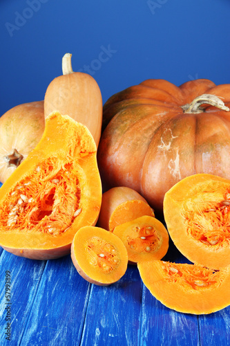 Ripe cut pumpkins on wooden table on blue background