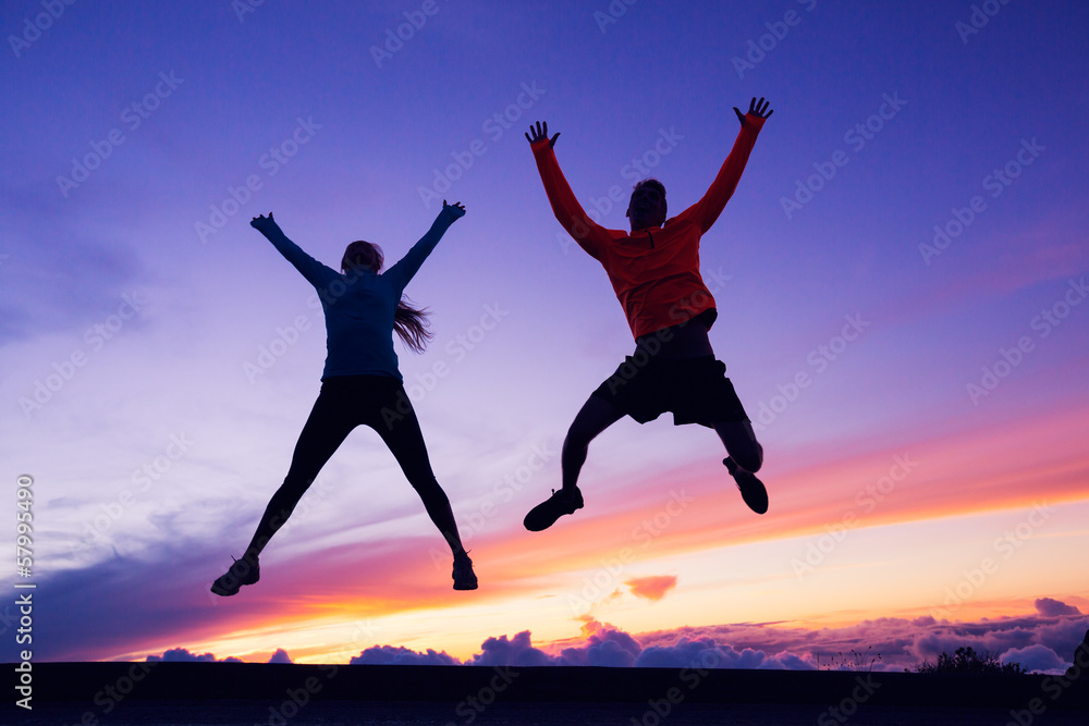 Fototapeta premium Happy man and woman having fun jumping into air at sunset