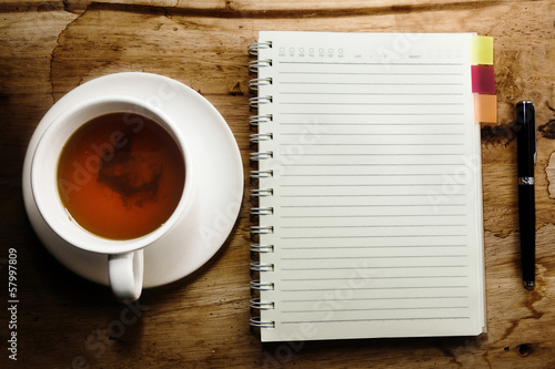 Tea cup, spiral notebook and pen on the wooden table background