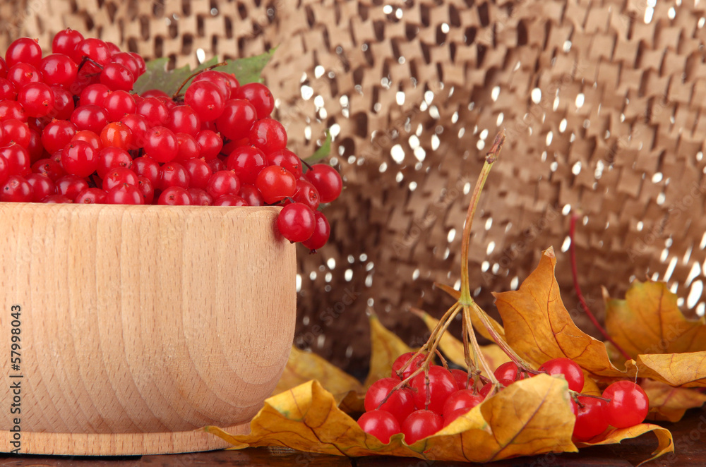 Red berries of viburnum in wooden bowl with yellow leaves