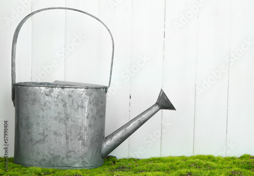 Watering can on grass on wooden background