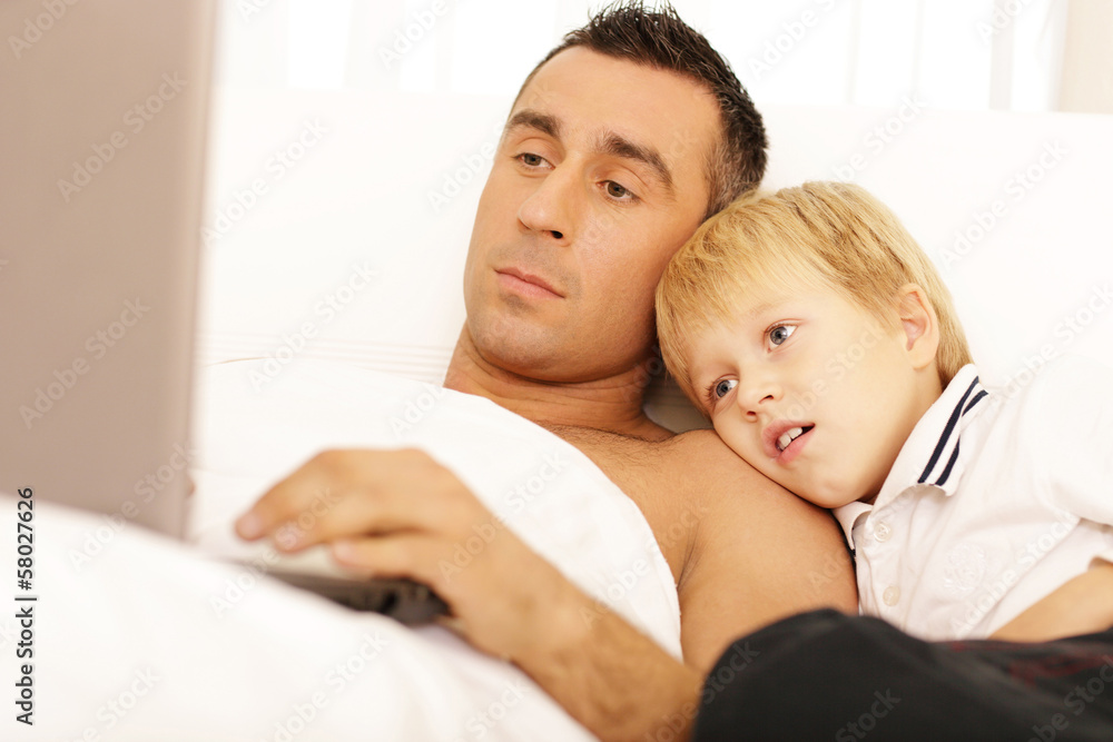 Father and son surfing on their computers on the bed at home Father and son surfing on their computers on the bed at home