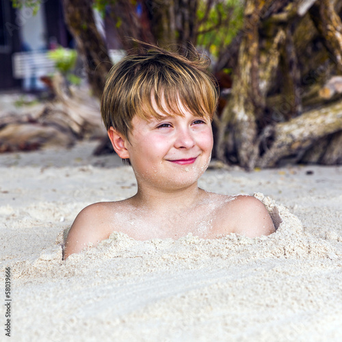 young boy covered by fine sand at the beach