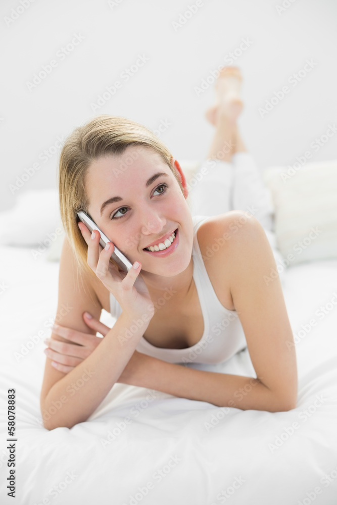 Cute blonde woman phoning with her smartphone lying on her bed Cute blonde woman phoning with her smartphone lying on her bed