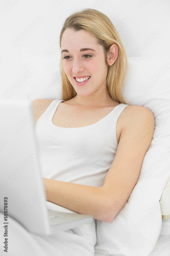 Content young woman working with her notebook lying on her bed Content young woman working with her notebook lying on her bed