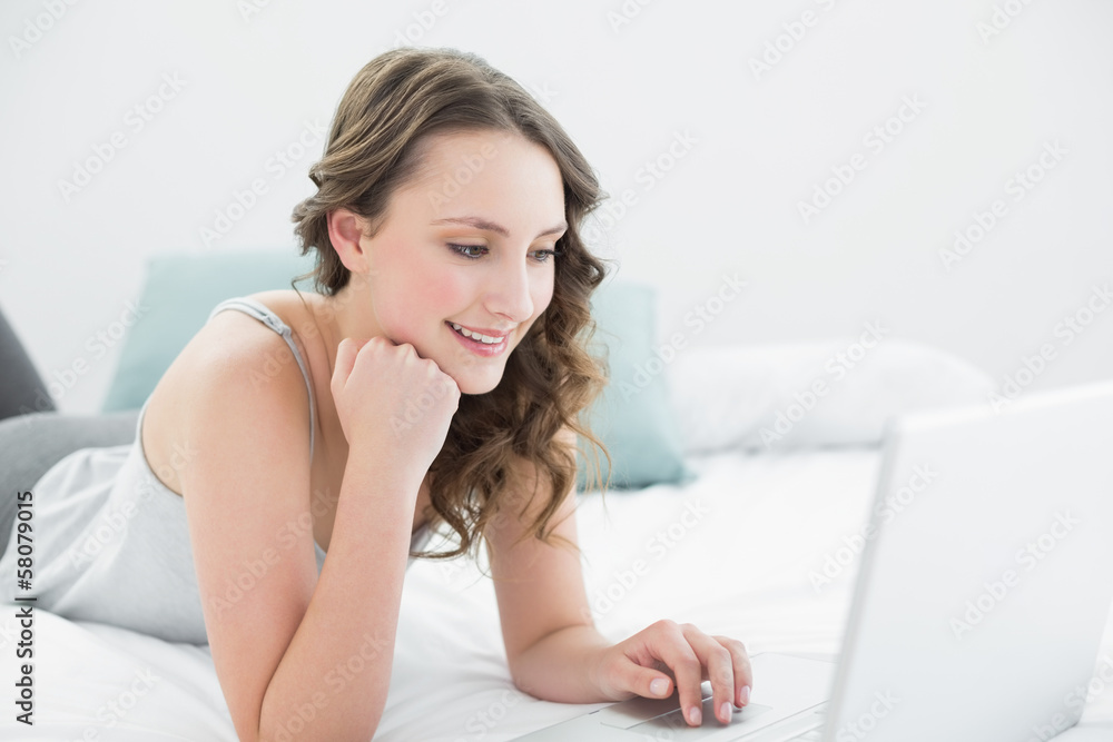 Smiling casual brunette using laptop in bed Smiling casual brunette using laptop in bed