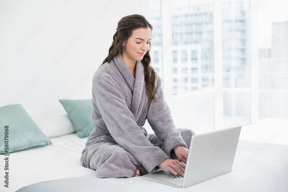 Brunette in bathrobe using laptop in bed