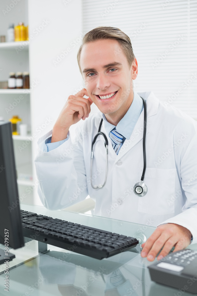 Smiling male doctor sitting with computer at medical office Smiling male doctor sitting with computer at medical office