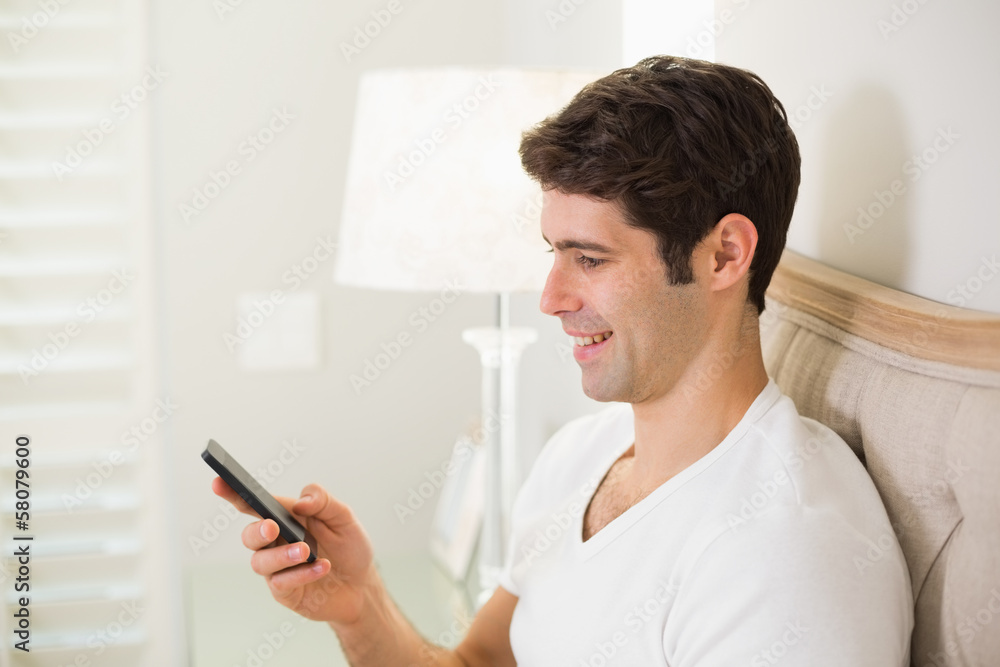 Casual smiling young man text messaging in bed Casual smiling young man text messaging in bed