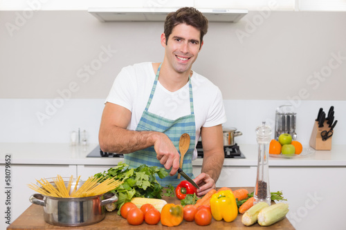 Smiling young man chopping vegetables in kitchen